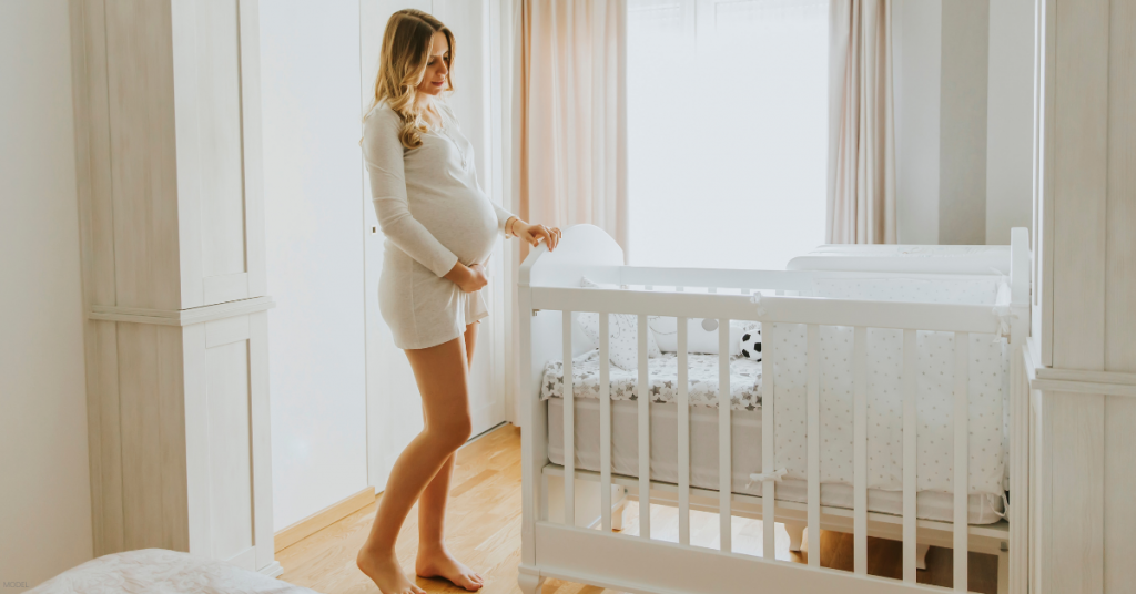 A pregnant woman stands in her baby's room.