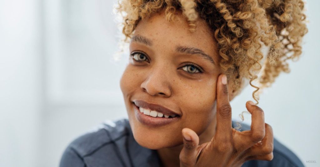 Woman with clear, wrinkle-free skin (model) examining her BOTOX® results in the mirror.